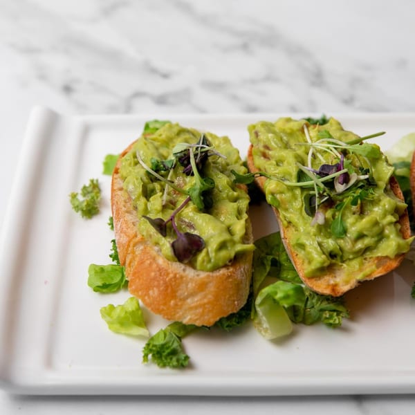 Two avocado toasts with microgreens on a white rectangular plate with lettuce garnish.