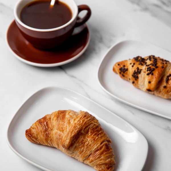 A cup of coffee and two croissants, one plain and one with chocolate sprinkles, on a marble surface.