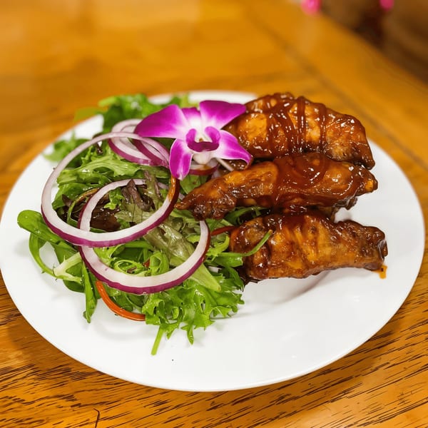 Azara Kitchen's African BBQ chicken wings with salad, red onion, and an orchid garnish.
