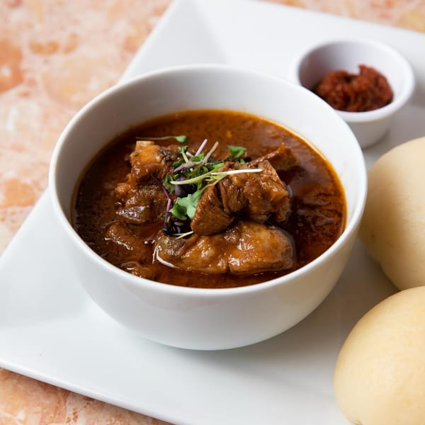 Azara Kitchen's African stew with meat, garnished with microgreens, served with buns and a side of sauce.