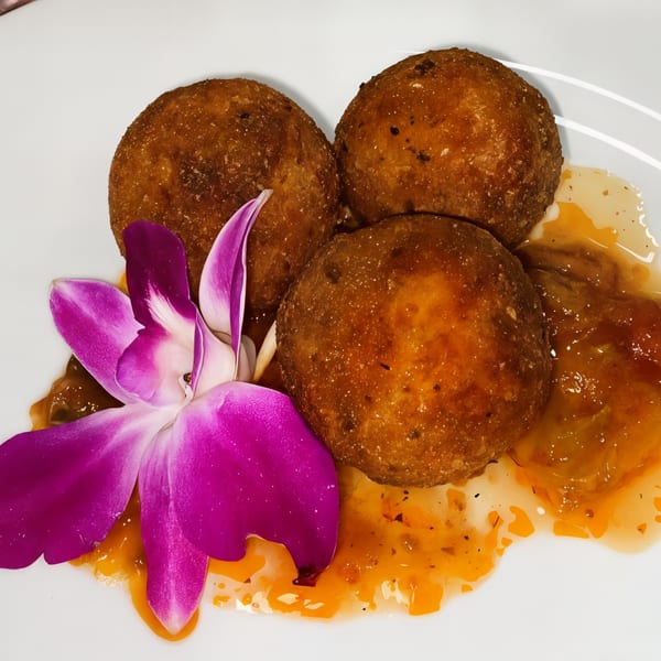 Three golden-brown fried balls, drizzled with orange sauce and garnished with a purple orchid.